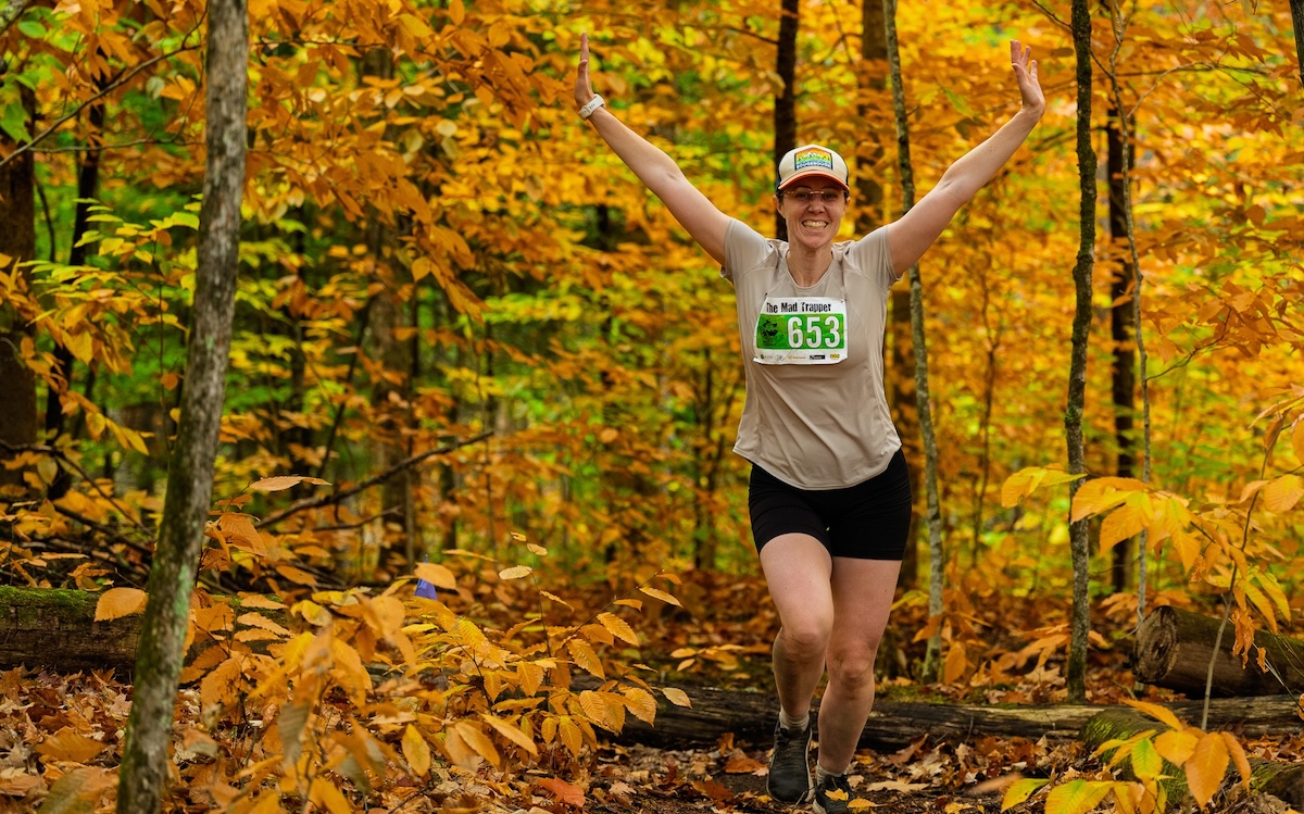 A smiling trail runner celebrates among autumn leaves